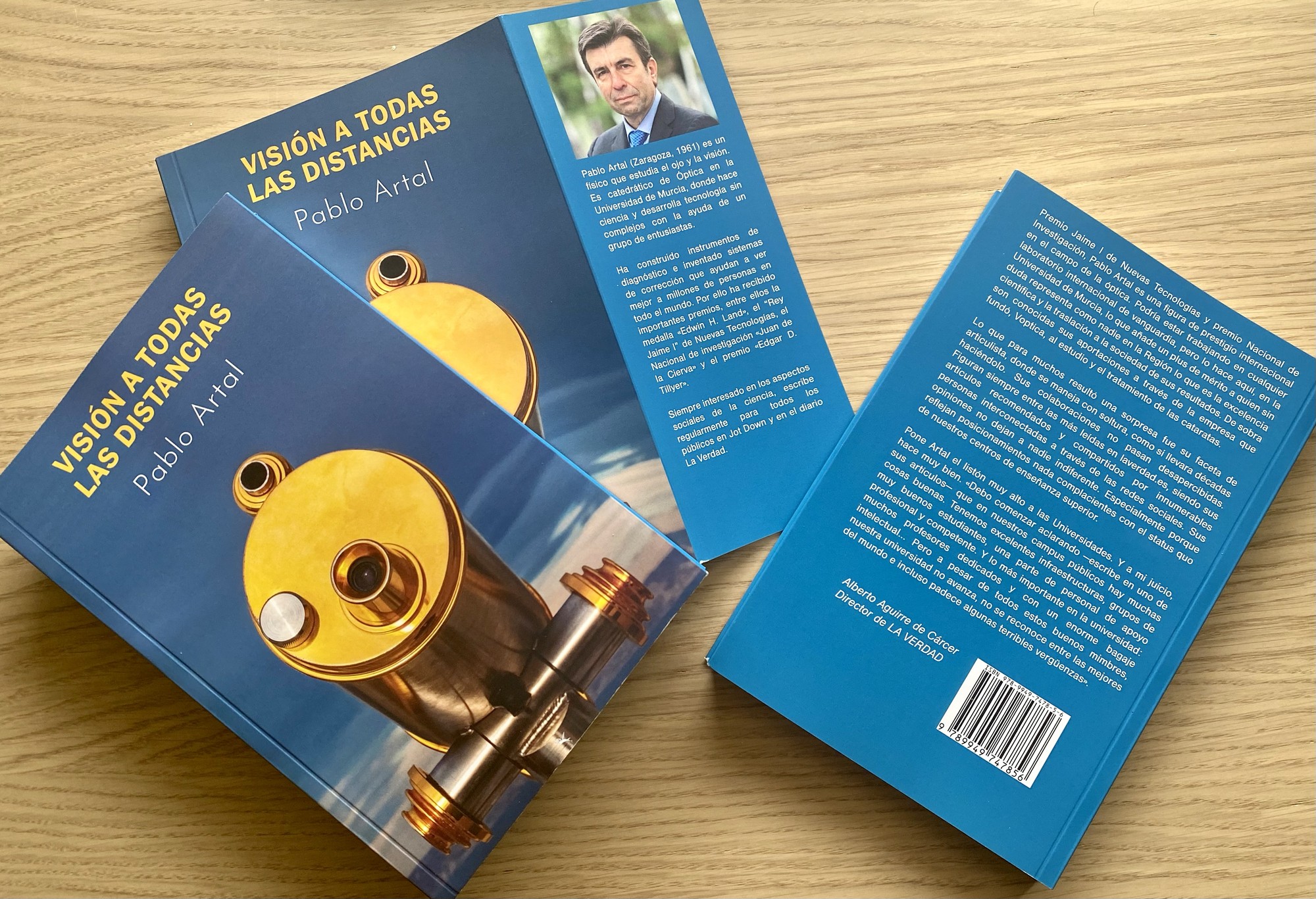 Several copies of Visión a todas las distancias by Pablo Artal, with blue covers, on a wooden table.