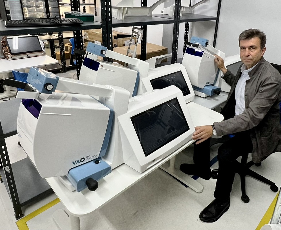Pablo Artal seated alongside several Voptica VAO systems, with their screens and optical units on a table.